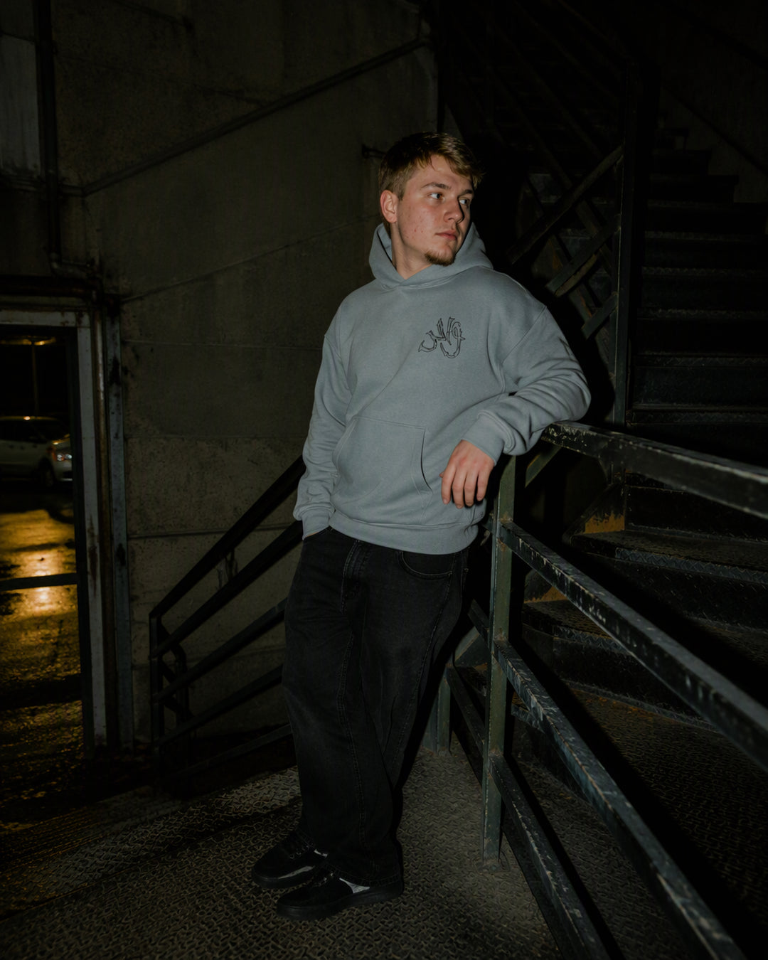 Gray Wahid hoodie on a supplied digitally created model beside outdoor stairs